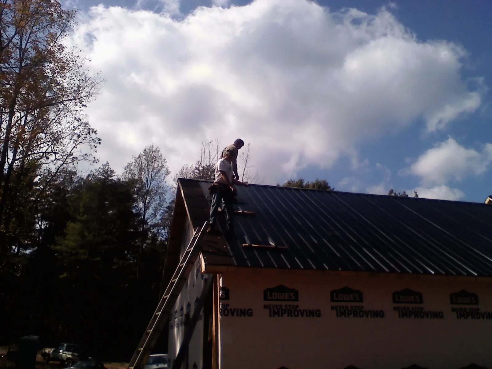 Roofer fastening dark metal panels high against a cloudy sky, from a Roof Inspection job in Wildwood