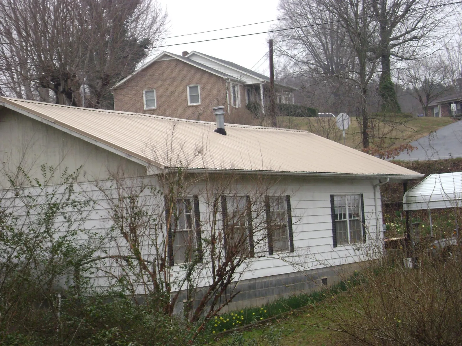 Tan metal roof on a white sided house set into a hillside — Commercial Roofing by Roofing Brothers in Wildwood